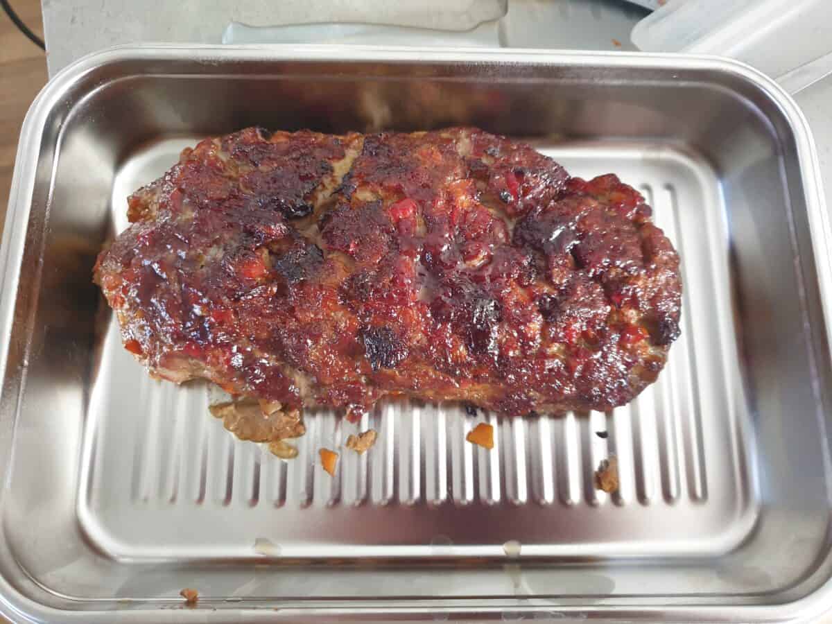 An Air Fryer Meatloaf with a caramelized, slightly charred glaze on top sits freshly cooked in a rectangular metal roasting pan with a ridged bottom.