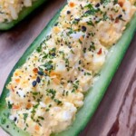 Egg Salad Cucumber Boats feature a halved cucumber filled with creamy egg salad, topped with chopped herbs and seasoning, and served on a wooden board.