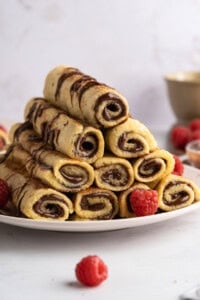 A plate stacked with chocolate-filled French Toast Rollups, drizzled with chocolate sauce and garnished with fresh raspberries.