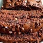 Close-up of thick slices of moist chocolate banana bread recipe topped with chocolate chips, displayed on a white plate. The bread looks rich, dense, and studded with chocolate chips throughout.
