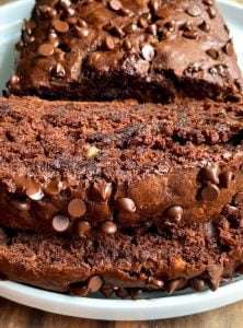 Close-up of thick slices of moist chocolate banana bread recipe topped with chocolate chips, displayed on a white plate. The bread looks rich, dense, and studded with chocolate chips throughout.