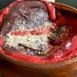 A wooden bowl filled with dark chocolate, bright red berry sauce, and a sprinkle of crushed nuts, this dessert resembles a decadent strawberry smoothie bowl with its rich flavors and vibrant presentation.