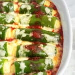 A white baking dish with jalapenos topped with melted cheese, arranged neatly in rows on a layer of tomato sauce.