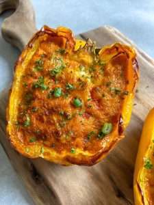 A yellow bell pepper half, filled with a golden-brown cheesy Breakfast Stuffed Peppers filling and garnished with chopped herbs, sits on a wooden cutting board.