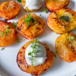 A white plate with Air Fryer Peaches—grilled halves, some topped with a scoop of vanilla ice cream and fresh herb sprigs as garnish.