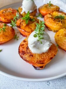 Grilled peach halves on a white plate, topped with scoops of vanilla ice cream and garnished with fresh herbs, served alongside crispy Air Fryer Radishes for a delightful mix of flavors.