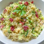 A white bowl filled with Cranberry Quinoa Salad, garnished with parsley. The salad contains chopped cucumber and pieces of dried cranberries, creating a colorful and fresh appearance.