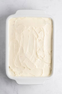 A white rectangular dish filled with smooth, swirled frosting on a light marble surface.