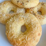 Four homemade bagels with golden crusts sit on a white plate. Made using an Easy Bagel Recipe, two are topped with sesame seeds and two with an everything seasoning blend.