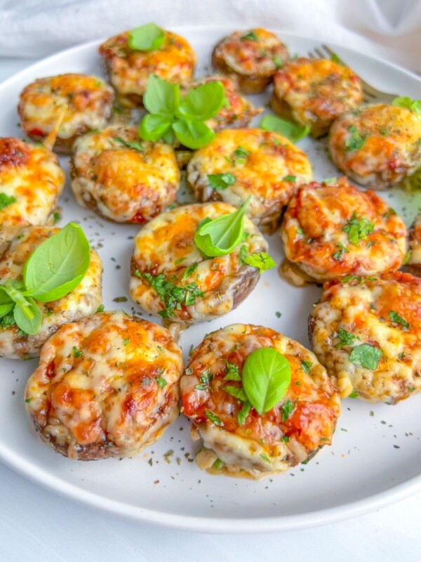 A white plate filled with baked stuffed mushrooms topped with melted cheese, chopped herbs, and garnished with fresh basil leaves.