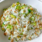 A white bowl filled with Zucchini Rice—cooked white rice mixed with chopped zucchini, ground meat, grated carrots, and topped with fresh green herbs—makes for a perfect meal prep easy meal.