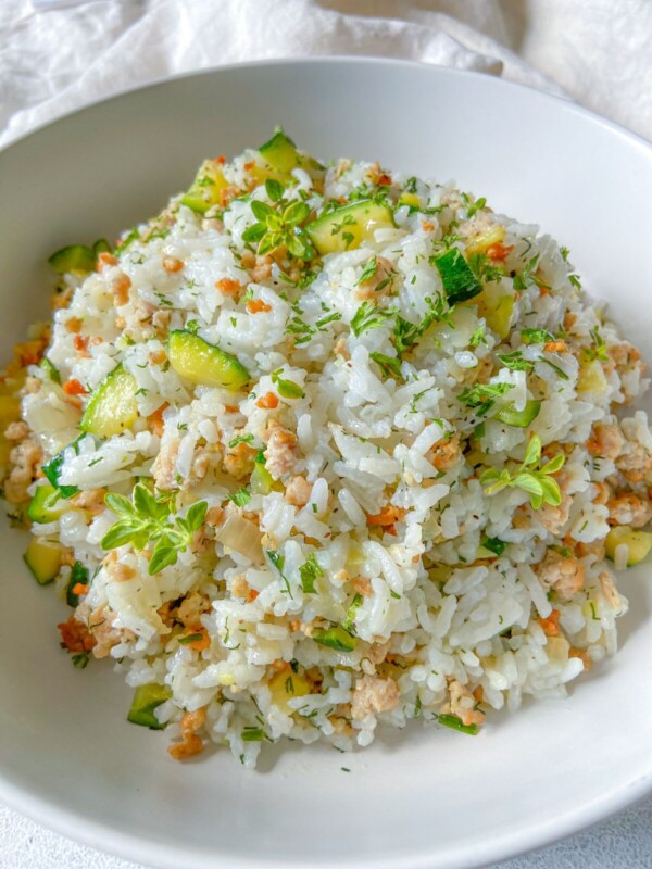 A white bowl filled with Zucchini Rice—cooked white rice mixed with chopped zucchini, ground meat, grated carrots, and topped with fresh green herbs—makes for a perfect meal prep easy meal.
