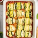 Baked Zucchini Lasagna Rolls filled with cheese and herbs, arranged neatly in a white casserole dish on a bed of marinara sauce, and garnished with chopped parsley.