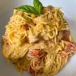 A close-up of creamy Spaghetti Squash Pasta with cherry tomatoes, garnished with a sprig of fresh basil, served in a white bowl.