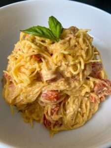 A close-up of creamy Spaghetti Squash Pasta with cherry tomatoes, garnished with a sprig of fresh basil, served in a white bowl.