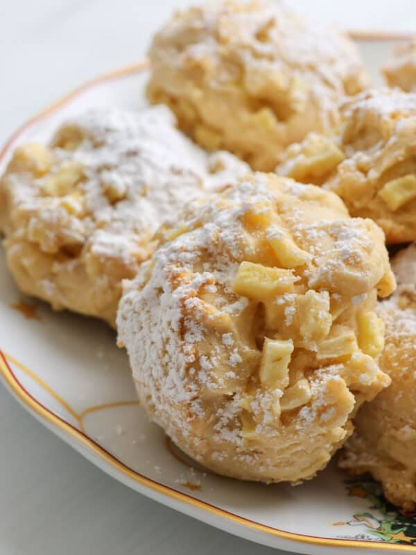Close-up of apple fritters and Apple Cookies (Scones) dusted with powdered sugar, arranged on a decorative plate. The fritters have a golden, crispy texture with visible apple pieces. - 6