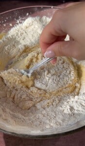 A hand holding a fork mixes flour with a wet dough mixture in a bowl, starting the process of combining ingredients for baking delicious Apple Cookies (Scones).