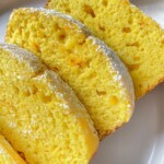 Three slices of moist Orange Lemon Cake with a light dusting of powdered sugar on top, arranged on a white plate. The cake appears soft and fluffy, with a slightly golden crust.