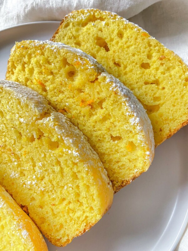 Three slices of moist Orange Lemon Cake with a light dusting of powdered sugar on top, arranged on a white plate. The cake appears soft and fluffy, with a slightly golden crust.