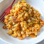 A white bowl filled with seasoned white beans garnished with chopped herbs, served with a reddish-brown fork on the side.