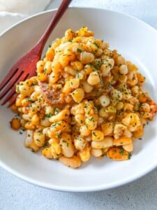 A white bowl filled with seasoned white beans garnished with chopped herbs, served with a reddish-brown fork on the side.