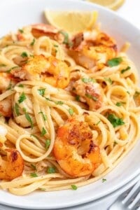 A plate of Lemon Shrimp Pasta featuring linguine topped with grilled shrimp, garnished with fresh parsley and served with a lemon wedge.