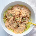 A white bowl filled with chopped lettuce, ground beef, and a generous layer of creamy orange Big Mac Salad sauce, garnished with herbs. A yellow fork rests in the bowl, which sits on a white surface next to a light napkin.