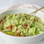 A white bowl filled with a green salad topped with crumbled meat and drizzled with a creamy green dressing—perfect for using fresh greens after learning how to dry herbs—rests beside a fork ready for your first bite.