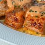 Close-up of Mac Sauce Salmon: three pieces of grilled salmon topped with a creamy orange sauce and fresh herbs, served on a white plate.