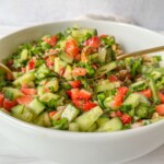 A white bowl filled with Strawberry Spinach Salad made of chopped cucumbers, strawberries, leafy greens, and walnuts, with a fork resting inside.