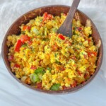 Golden tofu scramble with onions and roasted bell peppers in a skillet, turmeric hue.