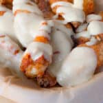 Alfredo Chicken Wings in a parchment-lined tray are being topped with a generous drizzle of creamy white sauce.