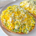 A close-up of toast topped with a layer of avocado and finely grated hard-boiled egg, garnished with herbs, alongside crispy Pasta Chips on a white plate.