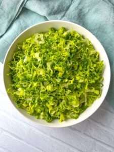 A white bowl filled with finely shredded green lettuce sits on a light surface with a light blue cloth nearby, perfect for demonstrating how to shred lettuce effortlessly.