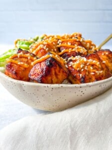 A beige speckled bowl filled with grilled, glazed chicken meatballs on white rice—similar to a delicious Vegetable Fried Rice Recipe—topped with shredded carrots, sesame seeds, nori strips, and avocado slices on the side.