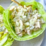 A close-up of Chicken Lettuce Cups featuring creamy chicken salad with diced vegetables, served in fresh lettuce leaves and garnished with a small white edible flower, on a beige plate.