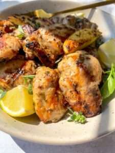 A plate of herb marinated chicken pieces garnished with fresh herbs and served with lemon wedges, bathed in natural sunlight.