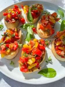A plate of Italian Bruschetta featuring toasted bread slices topped with diced red and yellow tomatoes, garnished with fresh basil leaves and microgreens, served on a white plate.