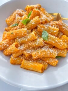 A white bowl filled with rigatoni pasta coated in creamy orange tomato sauce, topped with grated parmesan and fresh basil—a classic from The Modern Nonna, perfect if you're searching for easy meal ideas inspired by European recipes.