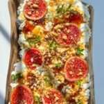 A wooden board topped with whipped ricotta, fresh figs, chopped nuts, honey drizzle, and green herbs—an artistic take inspired by the viral goat cheese board trend, beautifully arranged on a white background.