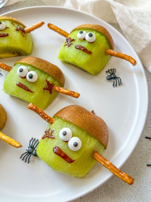 Sliced kiwis decorated as Frankenstein faces with candy eyes, chocolate-drawn mouths and scars, kiwi skin as hair, and pretzel sticks as bolts are a spooky treat—perfect alongside halloween mummy hotdogs for your festive celebration.