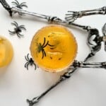 A top view of a yellow drink with a sugared rim and plastic black spider decorations, placed on a silver skeleton prop, showcases one of the best simple Halloween cocktails in a festive, spooky setting.