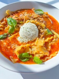 A bowl of Lasagna Soup with ruffled pasta, tomato broth, ground meat, fresh basil leaves, and a scoop of ricotta cheese in the center.