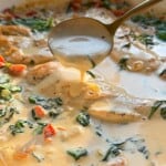 A spoon scoops creamy soup from a bowl, filled with chunks of vegetables and greens. The soup's surface shows a rich, smooth texture with hints of herbs, offering a warm, inviting appearance.