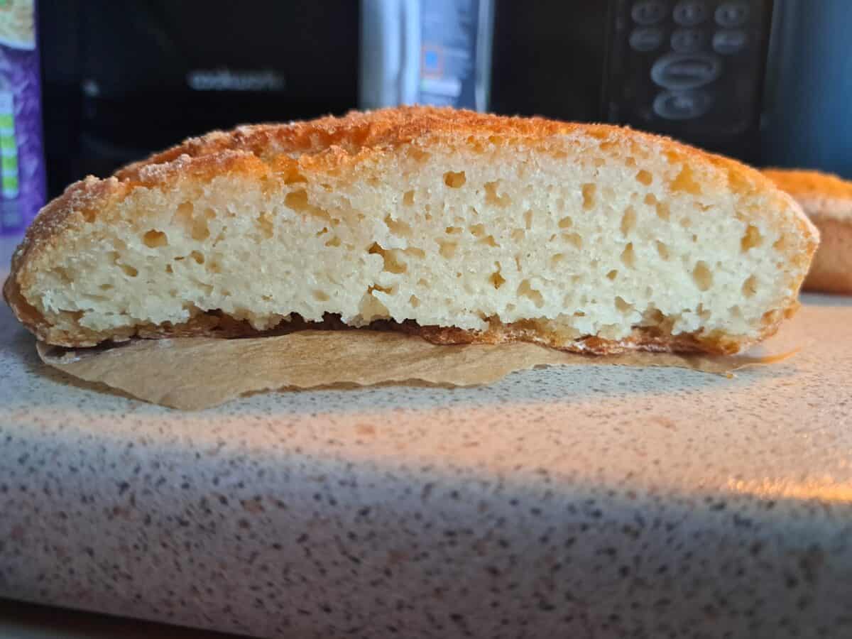 A close-up of a sliced, golden-brown loaf with a dense, moist crumb on a kitchen countertop, resting on a piece of parchment paper.