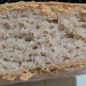 Close-up of a sliced piece of bread with a golden crust and a soft, airy interior, showing a network of small holes throughout, indicating a light and fluffy texture.