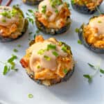 Five Chicken Bake Cups wrapped in seaweed, topped with creamy sauce and chopped green onions, are arranged on a white plate with sprigs of fresh herbs.