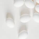 Several white eggs are scattered across a light, neutral background, creating a minimalistic and clean appearance—perfect for illustrating techniques like how to cut deviled eggs. Soft shadows add depth to the composition.