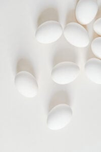 Several white eggs are scattered across a light, neutral background, creating a minimalistic and clean appearance—perfect for illustrating techniques like how to cut deviled eggs. Soft shadows add depth to the composition.