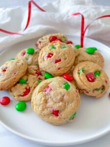 A plate of holiday cookies with red and green candy-coated chocolates, displayed on a white surface with a red ribbon in the background, brings festive flair to any Holiday Charcuterie Board.